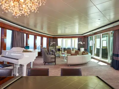 Eine geräumige, luxuriöse Suite der Norwegian Gem mit großem weißen Flügel, bequemen Sitzbereichen und Panoramafenstern zum Meer.