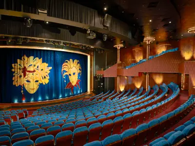 Das festliche Stardust Theater an Bord der Norwegian Gem mit leeren blauen Samtsitzen. Der blaue Buehnenvorhang zeigt goldene venezianische Masken.