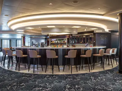 Eine moderne, runde Bar an Bord der Norwegian Getaway mit vielen Spirituosenregalen. Braune Barhocker stehen um die helle Theke. Ein Starbucks-Logo ist im Hintergrund erkennbar.