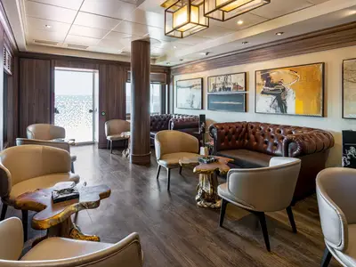 Stilvolle Zigarren-Lounge an Bord der Norwegian Getaway. Der Raum ist mit braunen Ledersofas, hellen Sesseln und einzigartigen Holztischen eingerichtet. Abstrakte Kunstwerke zieren die Wände, und durch eine Glastür ist das Meer zu sehen.