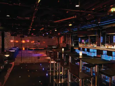 Nachtclub "Bliss" an Bord der Norwegian Getaway. Rote LED-Wände, eine lange, blau beleuchtete Bar mit Flaschen. Moderne Tische, Stühle und ein glänzender Boden reflektieren die Lichter.