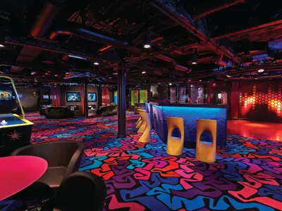 Der Jugendclub Entourage der Norwegian Getaway ist mit einer leuchtenden Bar, Spielautomaten und Airhockey ausgestattet. Farbiger Teppich und Neonlicht prägen die moderne Atmosphäre.