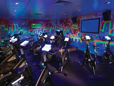Modernes Spinning-Studio an Bord der Norwegian Getaway mit vielen Fahrrädern. Wände mit leuchtenden Graffiti-Motiven und Sprüchen wie 'POWER'. Eine dynamische Trainingsatmosphäre.