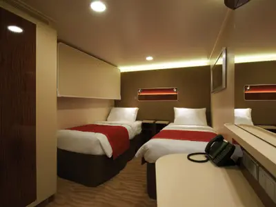 Eine gemütliche Innenkabine an Bord der Norwegian Getaway mit zwei Betten, roter Bettwäsche, Schrank und Schreibtisch. Warme Beleuchtung betont die moderne Einrichtung der Kabine.