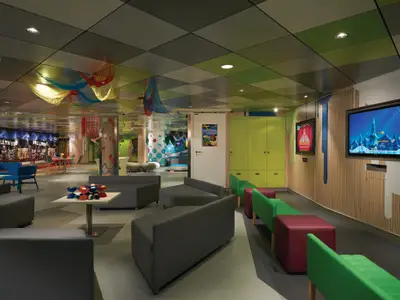 Weitläufiger, farbenfroher Kinderbereich Splash Academy an Bord der Norwegian Getaway. Viele Sitzgelegenheiten, Bildschirme und Spielzonen sind sichtbar. Die Decke ist mit bunten Stoffen dekoriert.