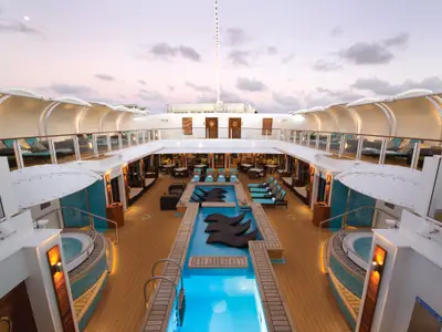 Poolbereich 'The Haven Courtyard' an Bord der Norwegian Getaway bei Abendstimmung. Beleuchtete Pools, Whirlpools und Lounge-Möbel auf dem Holzdeck.