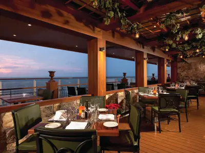 Das Spezialitätenrestaurant La Cucina Waterfront auf der Norwegian Getaway. Gedeckte Tische im eleganten Ambiente mit Meerblick bei Sonnenuntergang.