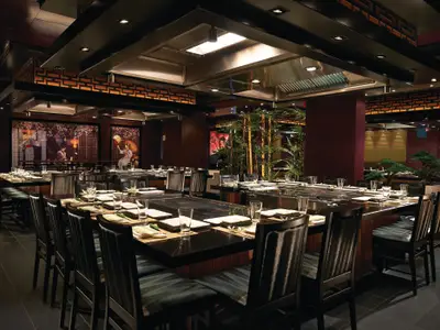 Das asiatisch inspirierte Teppanyaki-Spezialitätenrestaurant an Bord der Norwegian Getaway, mit mehreren Kochstationen, stilvoller Dekoration und Bambuspflanzen. Tische sind fuer Gaeste vorbereitet.