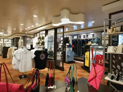 Moderne Boutique an Bord der Norwegian Getaway mit Auslagen von Kleidung, Handtaschen und Schmuck. Heller Verkaufsraum mit gemustertem Teppichboden.