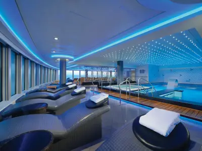 Die moderne Spa-Thermal-Suite an Bord der Norwegian Getaway. Blaue LED-Beleuchtung erhellt Pools, Whirlpools und ergonomische Liegen am Fenster mit Meerblick.