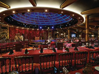 Das luxuriöse Illusionarium an Bord der Norwegian Getaway. Ein Spezialitätenrestaurant mit Showbühne, roten Tischen und einer blau beleuchteten Gitterdecke.