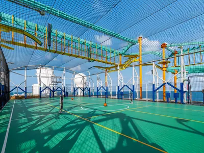 Blick auf den Sportplatz und Hochseilgarten unter freiem Himmel an Bord der Norwegian Getaway mit Blick auf das Meer. Der Platz ist grün markiert und hat einen Basketballkorb und ein Netz.