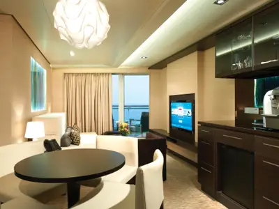 Blick in den eleganten Wohnbereich einer Suite an Bord der Norwegian Getaway, komplett mit Essbereich, Sofa, TV und Minibar. Ein Balkon bietet Meerblick.