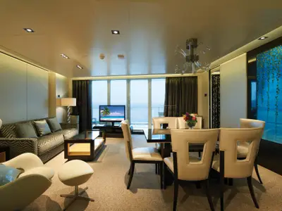 Geräumige Deluxe Owner's Suite an Bord der Norwegian Getaway. Die Suite umfasst einen eleganten Wohn- und Essbereich mit Meerblick durch große Fenster. Moderne Möbel und eine markante blaue Wandkunst sind zu sehen.