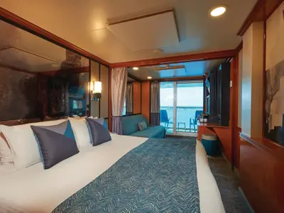 Moderne Balkonkabine an Bord der Norwegian Jade. Geräumiges Doppelbett mit blauen Kissen, Sofa und privater Balkon mit Meerblick. Helle Einrichtung mit Holz und Kunst. Gemütliche Atmosphäre.