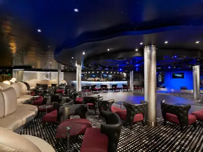 Die Bliss Lounge der Norwegian Jade. Eine moderne Bar, Tanzfläche und bequeme Sitzgruppen in Weinrot und Schwarz unter sternenbesetzter Decke.