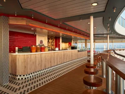 Moderne Pit Stop Bar an Bord der Norwegian Jade. Rote Kachelwand, helle Holztheke mit Getränken und Barhocker auf einem Deck mit Meerblick.