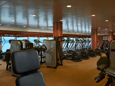Geräumiges Fitnesscenter an Bord der Norwegian Jade mit vielen modernen Trainingsgeräten und großen Fenstern, die Meerblick bieten.