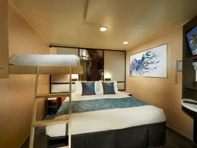 Eine moderne Innenkabine an Bord der Norwegian Jade mit einem Doppelbett, einem darüber liegenden Hochbett, einem großen blauen Kunstwerk an der Wand und einem Fernseher.