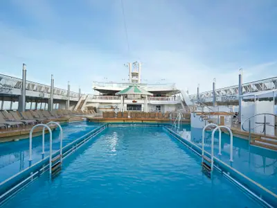 Das Pooldeck der Norwegian Jade: Ein langer blauer Swimmingpool umgeben von Liegestühlen und den oberen Decks. Klarer Himmel, tageslicht, keine Personen.