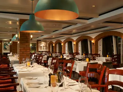 Das Spezialitätenrestaurant La Cucina an Bord der Norwegian Jade. Gedeckte Tische mit Gläsern und Kerzen, Ziegelsteinwände und warme Beleuchtung schaffen ein gemütliches Ambiente.