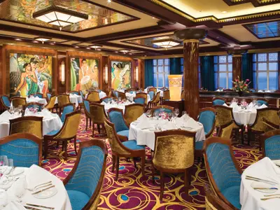 Innenansicht des Grand Pacific Restaurants auf der Norwegian Jade mit zahlreichen, weiss gedeckten Tischen und blauen sowie goldenen Stühlen. Die Wände sind mit farbenprächtigen Gemälden verziert.
