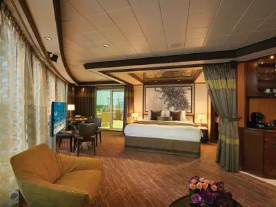Helle, moderne Owners Suite an Bord der Norwegian Jade. Das große Doppelbett steht im Zentrum, umgeben von einem Sitzbereich und Zugang zu einem möblierten Balkon.