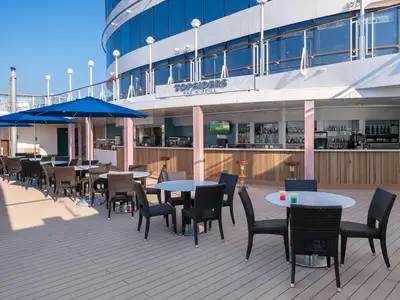 Die Topsiders Bar & Grill an Bord der Norwegian Jewel mit Tischen, Stühlen unter blauen Sonnenschirmen und einer gut ausgestatteten Bar.