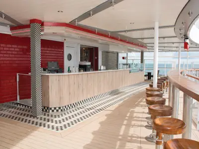 Der 'Jewel Pit Stop' an Bord der Norwegian Jewel: eine stylische Bar mit roten Ziegelwänden, schwarz-weiß kariertem Boden und Holzhockern am Tresen mit Meerblick.