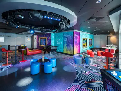 Blick in den farbenfrohen 'Entourage' Teen Club der Norwegian Jewel. Der Raum ist mit modernen Möbeln, Kicker, beleuchteten Wänden und grafischem Teppichboden ausgestattet. Ohne Personen.