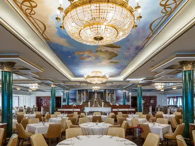 Panoramablick in den opulenten Speisesaal Tsars Palace der Norwegian Jewel. Zahlreiche Tische, beeindruckende Kronleuchter und eine Deckenmalerei mit Engeln prägen den Raum.