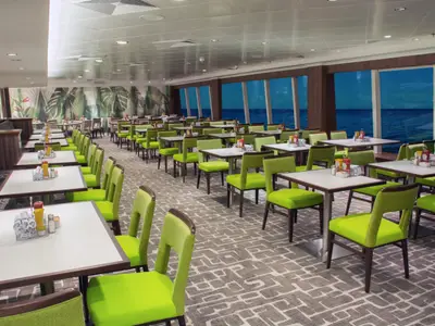 Innenansicht des weitläufigen Garden Café Buffetrestaurants an Bord der Norwegian Jewel. Zahlreiche Tische mit grünen Stühlen und großen Panoramafenstern mit Blick auf das blaue Meer.