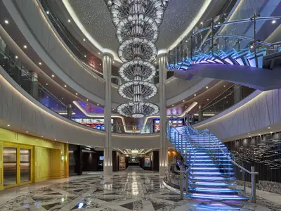 Atrium der Norwegian Joy mit imposantem Kronleuchter und beleuchteter Treppe. Mehrere Ebenen mit Glasbalkonen und Casino-Bereich. Modernes und luxuriöses Interieur.