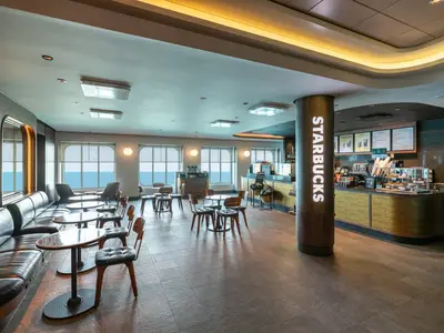 Das moderne Starbucks-Café an Bord der Norwegian Joy. Der Innenraum zeigt eine Bar, Tische und bequeme Ledersofas mit Blick auf das offene Meer.