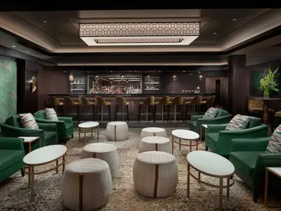 Blick in die elegante Maltings Whiskey Bar an Bord der Norwegian Joy. Im Vordergrund bequeme grüne Sessel, Tische und Hocker. Dahinter die lange Bar mit zahlreichen Flaschen und Hockern.