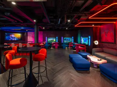 Die Entourage Gaming-Lounge an Bord der Norwegian Joy mit farbiger Neonbeleuchtung, verschiedenen Spielstationen und modernen Sitzbereichen in Blau, Rot und Pink.
