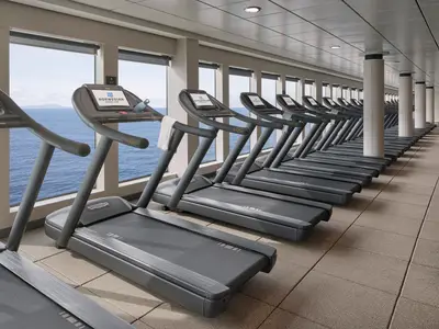 Eine lange Reihe moderner Technogym-Laufbänder im Fitnesscenter der Norwegian Joy mit großen Fenstern zum offenen Meer.