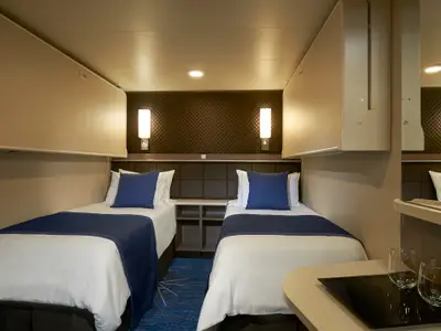 Moderne und helle Innenkabine der Norwegian Joy. Zwei Einzelbetten mit blauen Kissen, hochklappbare Zusatzbetten darüber. Funktionale Einrichtung.