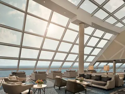 Die helle Horizon Lounge an Bord der Norwegian Joy mit grossen Glasfenstern, die einen Panoramablick auf das Meer und den Himmel bieten. Gemuetliche Sitzgruppen laden zum Verweilen ein.