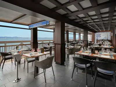 Innenansicht des Restaurants La Cucina an Bord der Norwegian Joy. Elegante Holzeinrichtung, blaue Azulejo-Wandkunst und gedeckte Tische mit weitem Meerblick.