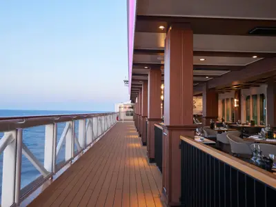 Elegantes Spezialitätenrestaurant La Cucina an Bord der Norwegian Joy. Holzdeck mit Tischen, Stühlen und Meerblick. Gedeckte Tische laden zum Verweilen ein.