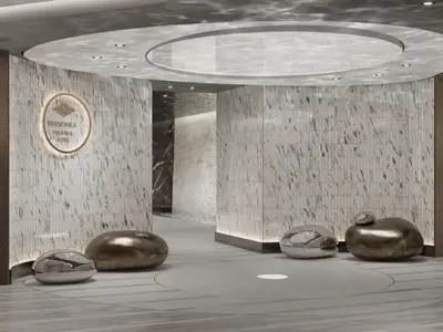Der moderne Eingangsbereich der Mandara Thermal Suite an Bord der Norwegian Joy. Heller Raum mit geschwungenen Wänden, gemusterten Fliesen und glänzenden, organisch geformten Skulpturen auf dem Boden.