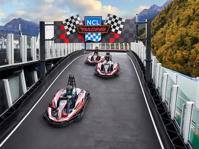Drei Personen fahren Go-Karts auf der Rennstrecke an Bord der Norwegian Joy. Die mehrstufige Bahn bietet ein aufregendes Erlebnis mit malerischer Berg- und Herbstlandschaft im Hintergrund.