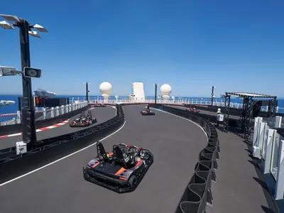 Eine Go-Kart-Rennstrecke an Bord der Norwegian Joy. Mehrere elektrische Karts stehen auf dem Rundkurs im Freien auf dem obersten Deck. Im Hintergrund sind das blaue Meer und der Himmel zu sehen.