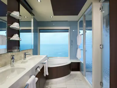 Ein modernes Badezimmer an Bord der Norwegian Joy mit zwei Waschbecken, Badewanne am Fenster und separater Dusche. Heller Raum mit Meerblick.