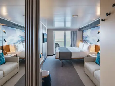 Innenansicht einer geräumigen Balkonkabine an Bord der Norwegian Luna. Ein großes Bett mit weißen Decken, ein Sofa, ein Schreibtisch und ein Balkon mit Meerblick sind zu sehen.