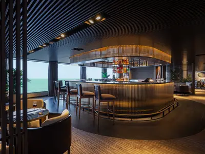 Eine moderne Bar-Lounge an Bord der Norwegian Luna mit elegantem, beleuchtetem Bartresen und bequemen Sitzgelegenheiten. Große Fenster zeigen den Meerblick.