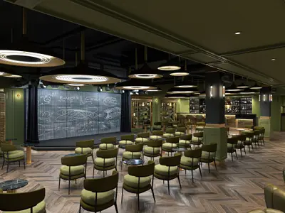 Die Improv Bar und Lounge an Bord der Norwegian Luna zeigt eine Bühne mit Bildschirm, grüne Sessel, kleine Tische und eine Bar. Warme Beleuchtung sorgt für eine gemütliche Atmosphäre.