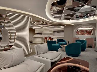 Bar-Lounge auf der Norwegian Luna. Geschwungene, beleuchtete Wände, wellenförmige Bar und farbige Sessel. Ein Hängesessel und gespiegelte Deckenbereiche sind sichtbar.