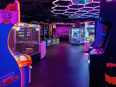 Eine neonbeleuchtete Game Zone an Bord der Norwegian Luna mit verschiedenen Arcade-Automaten. Pinke und blaue Lichter tauchen den Raum in eine futuristische Atmosphäre. Kein Personal oder Gäste sind zu sehen.